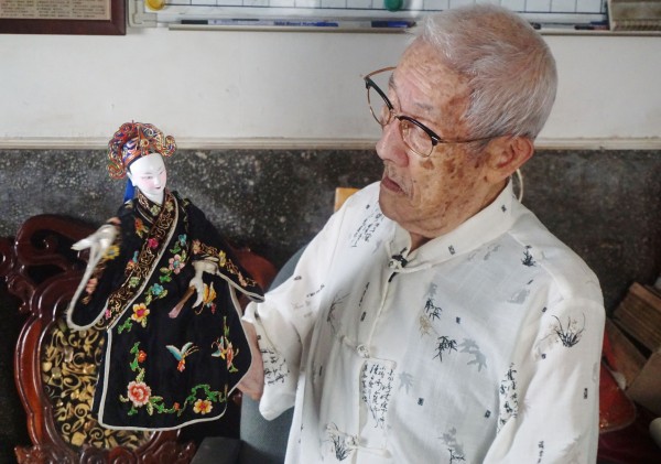 Master Chen holds one of his elaborately dressed and delicate dolls up.